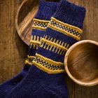 Dunkelblaue Stricksocken mit gelben Mustern liegen auf einer Holzplatte, umrahmt von hölzernen Schüsseln.