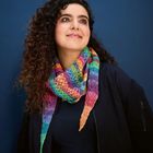 Ich kenne die Person nicht. Eine Frau mit lockigem Haar trägt einen bunten Schal vor einem blauen Hintergrund.