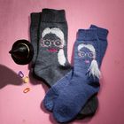 "Pop!" ist auf zwei gestrickten Socken mit Gesichtsmotiven. Links ein Miniaturhexenhut und bunte Marker auf rosa Hintergrund.