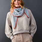 Person mit rotem Haar trägt einen gestreiften Schal und grauen Pullover. Wand im Hintergrund ist dunkelgrau.