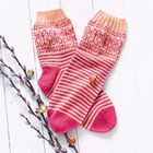 Zwei gestrickte Socken in Rot- und Pinktönen mit Mustern, daneben Weidenkätzchen mit bunten Vögeln.