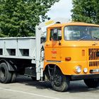 Aufschrift "ESR Rostock" auf einem orangefarbenen LKW mit Kran, im Hintergrund Bäume.