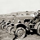 Mehrere Männer sitzen auf einer Reihe von Traktoren auf einem Feld. Sie sind in Arbeitskleidung.