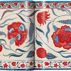 Rote und blaue Blumenmuster auf beigefarbenem Hintergrund, mit verzweigten Blättern und Blumenbordüre oben und unten.