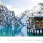 Text: "februar", Datumsliste. Eine Holzhütte am klaren Bergsee, umgeben von verschneiten Bergen und Nadelbäumen.