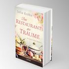 Auf einem Buchcover steht "Julia Kröhn, Das Restaurant der Träume, Historischer Roman". Blumen und Lebensmittel sind abgebildet.
