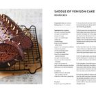 Rehrücken Kuchen mit Schokoladenglasur und Mandeldekoration auf einem Gitter. Rezept auf der rechten Seite.