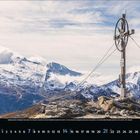 2 2024: Ein Gipfelkreuz mit Rädern vor einer schneebedeckten Berglandschaft, Kalenderdaten unten.