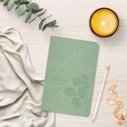 Text: "Zwischenbuch SIEBENEINUNDFÜNFZIG".  
Grünes Notizbuch, Eucalyptuszweig, gelbe Kerze, Bleistift, Stoff, helles Holz.