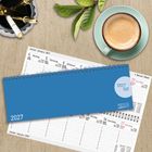 Kalender für 2027, zeigt Wochentage. Blauer Einband, Kaffeetasse und Stiftebehälter daneben.