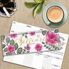 "Selfcare 2023" steht auf einem dekorativen Kalender mit pinken Blumen. Daneben eine Tasse Kaffee, Stifte und ein Blatt.