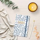 Notizheft mit Text "Everything starts with a new morning" und "2023". Umgebung: Eukalyptus, Kerze, Bleistift, Stoff.