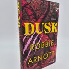 Auf dem Buchumschlag steht "DUSK ROBBIE ARNOTT". Das Design zeigt Bäume in rötlichen Tönen mit auffälligen Kratzspuren.
