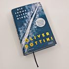 Auf einem Buchcover steht: "DIE SUMME ALLER DINGE", "OLIVER BOTTINI", "ROMAN". Ein Boot zieht eine Spur auf Wasser.