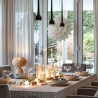 Ein festlich gedeckter Tisch mit Kerzen, Weingläsern und Tannenzweigen vor großen Fenstern und einem weißen Papierstern.