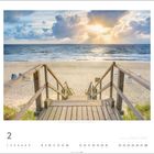 Im Februar führt ein hölzerner Steg zum Strand. Die Sonne strahlt hinter den Wolken über die See.