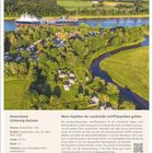 "ML RORO" auf einem Schiff im Wasser, umgeben von Feldern und einem Campingplatz mit Wohnmobilen, oben blauer Himmel.