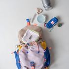 Eine bunte Tasche mit „bla bla bla“ auf einem Etui. Umgeben von Alltagsgegenständen wie Flasche, Kämmchen, und Seil.