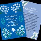 Vorne: "Leichtigkeit trägt dich, wohin du willst!" in Weiß auf Blau, umgeben von Blumenmotiven.