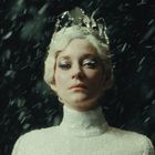 Eine Frau trägt eine glitzernde Krone und ein funkelndes weißes Kleid in einem Schneesturm.