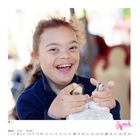 April mit Kalenderdaten. Ein lachendes Kind hält etwas in den Händen, Hintergrund verschwommen.