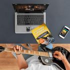 Text: "E-Gitarre lernen für Anfänger". Eine Person spielt Gitarre, mit Laptop und Smartphone auf einem Tisch.