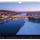 Februar-Kalenderblatt, verschneite Stadtlandschaft bei Dämmerung, Fluss, beleuchtete Brücke, Häuser und sanfte Hügel.