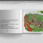 Seite 36. Figuren mit Mäuseohren in Wiese und roter Pflanze, sonniger Himmel im Hintergrund, Weg führt durch Wiese.