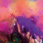 Keine Texte sichtbar. Menschen feiern, werfen lila und orangefarbenes Pulver in die Luft. Dynamisch und bunt.