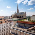 Farbenfrohes Dach mit Zickzack-Muster, historische Kathedrale im Hintergrund, helle Gebäudefassaden, blauer Himmel.