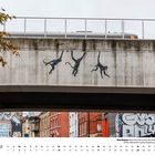 Ein Kalenderblatt für Oktober. Affen-Graffiti schwingt an Brücke in einer urbanen Umgebung voller Graffiti und Backsteinbauten.