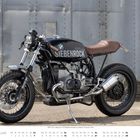 „SIEBENROCK 1070 sport“ auf schwarzem Motorradtank, darunter Kalender für Februar. Vintage-Motorrad vor metallener Wand.