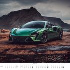 „FEBRUAR“ und „McLaren Artura“; grünes Auto auf verrostetem Boden vor einer bergigen Küstenlandschaft.