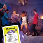Ein Raum mit tanzenden Menschen. Vordergrund: eine Karte mit "Challenge", "Magic Mike" und einer Tanzaufgabe.
