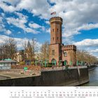Köln - Malakoffturm am Rheinhafen. Kalender für Februar 2027. Historischer Turm am Fluss unter blauem Himmel mit Wolken.