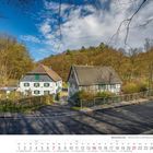 Kalender: Februar 2027. Fachwerkhäuser vor einem Wald. Klarer Himmel, gewundene Straße im Vordergrund.
