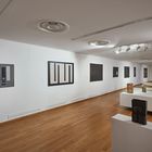 Galerie mit abstrakten Gemälden und minimalistischen Skulpturen, hölzerner Boden, weiße Wände und Deckenbeleuchtung.