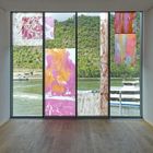 Blick aus einem Raum durch bunte Glaspaneele auf einen Fluss und bewaldete Hügel im Hintergrund.