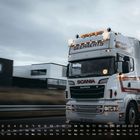 Text "GEEHAERTS" oben auf einem fahrenden weiß-roten Scania-Truck. Kalender unten.