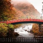 Text: "Shinkyō (Fußgängerbrücke) über den Fluss Daiya in der Stadt Nikkō". Rote Brücke über Fluss, umgeben von Herbstlaub.