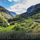 Flåmsbana, normalspurige Eisenbahnstrecke. Berglandschaft mit Wald, Fluss und einem Zug, der eine Kurve befährt.