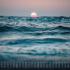 Kalender Februar, Mond über ruhigem Ozean bei Sonnenuntergang, Wellen im Vordergrund, pastellfarbener Himmel.