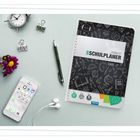 "Der Schulplaner 2026/27" steht auf dem Planer. Drumherum sind Uhr, Stift, Handy, Blumen und Kopfhörer arrangiert.