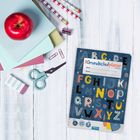 „Grundschulplaner 2026/27“ steht auf einem Planer mit bunten Buchstaben. Daneben liegen ein Apfel, Scheren und Schulsachen.