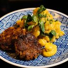 Teller mit zwei Frikadellen, Kartoffelsalat und Senf. Dekoriert mit Feldsalat. Teller hat blau-weißes Muster.