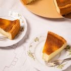 Zwei Stücke Käsekuchen auf verzierten Tellern, auf einem weißen Tischtuch mit Blumenstickerei.