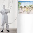 Links steht eine Person in einem weißen Schutzanzug mit Schläuchen, rechts ist eine botanische Illustration.