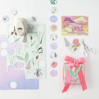 "The Sky is the Limit" auf einer Karte, daneben rosa Geschenk mit Schleife, Blumenillustrationen, Kreisgirlande, Schere.