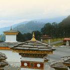 Oben steht "WEST-BHUTAN". Darunter sind traditionelle Stupas mit goldenen Spitzen und ein bewaldetes Bergpanorama.
