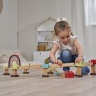 Ein kleines Mädchen spielt konzentriert mit einer Holzspielzeugbahn in einem hellen Zimmer.